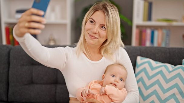 Anne ve kızı birbirlerine sarılıyorlar ve evde akıllı telefondan selfie çekiyorlar. - Fotoğraf, Görsel