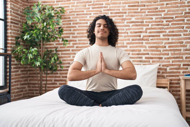 Young latin man doing yoga exercise sitting on bed at bedroom - Photo, Image