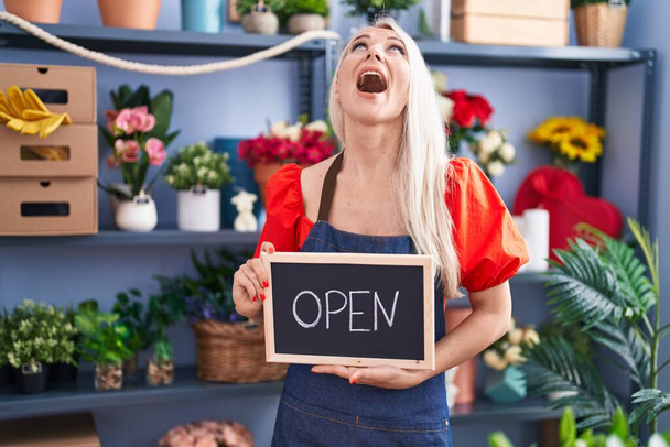 Caucasian woman working at florist holding open sign angry and mad screaming frustrated and furious, shouting with anger looking up.  - 写真・画像