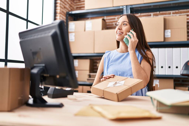 Młoda piękna latynoska kobieta e-commerce pracownik biznesu mówi na smartphone gospodarstwa pakiet w biurze - Zdjęcie, obraz