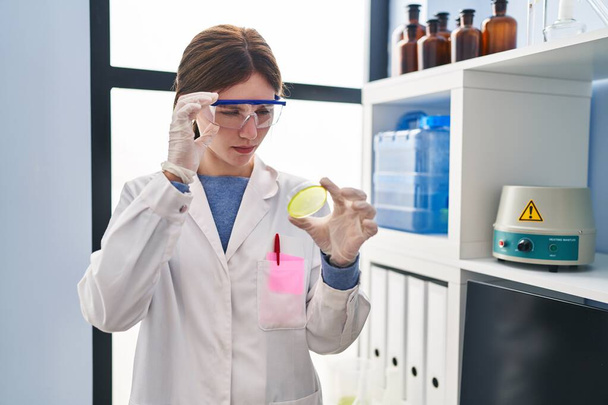 Nuori blondi nainen tiedemies etsii näyte vakava ilme laboratoriossa - Valokuva, kuva
