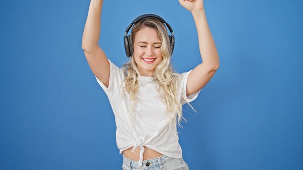 Mladá blondýna žena poslouchá hudbu a tanec přes izolované modré pozadí - Fotografie, Obrázek