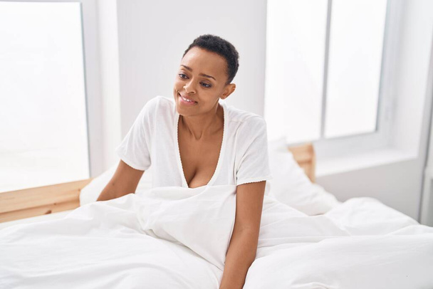 afro americano donna sorridente fiducioso seduta su letto a camera da letto - Foto, immagini