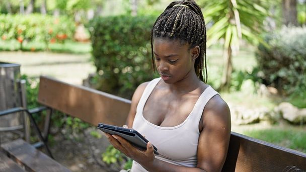African american woman using touchpad sitting on bench at park - Photo, Image