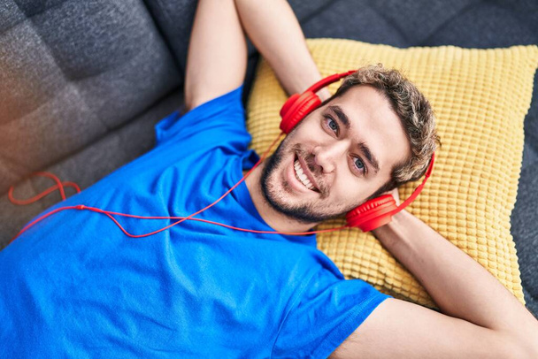 Young man listening to music lying on sofa at home - Foto, Imagen