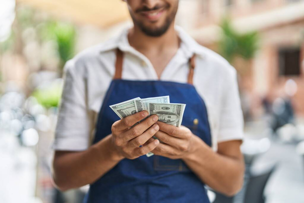 Young arab man waiter counting dollars working at restaurant - Foto, imagen