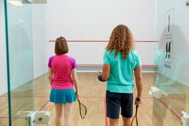 Mies ja nainen squash pelaaja tilalla maila näkymä takaa seisoo oviaukossa sisätiloissa urheilukenttä. Terveellisen ja aktiivisen elämäntavan käsite - Valokuva, kuva