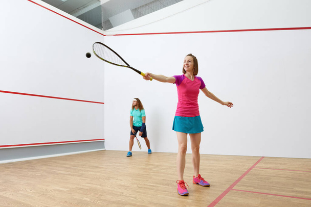 Feliz millennial-age pareja de personajes jugando juego de racquetball juntos. Jugadores de squash entrenando juntos en pista cubierta - Foto, imagen