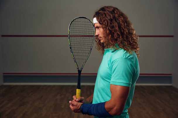 Młody, zadumany zawodnik z rakietą stojącą z tyłu. Trening gry w squasha na boisku. Profesjonalna koncepcja sportu i hobby - Zdjęcie, obraz