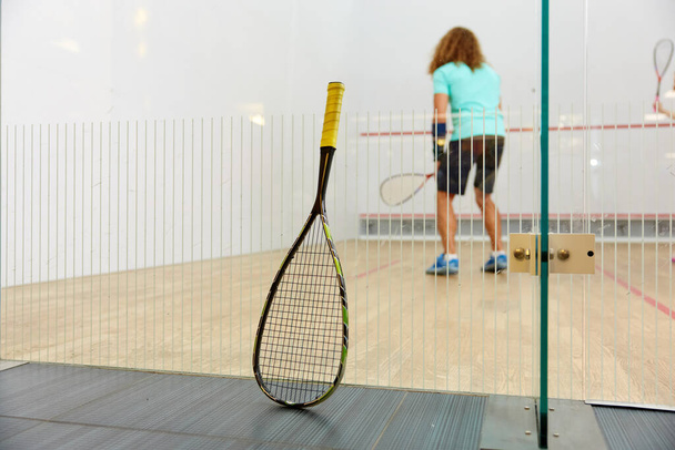 Racchetta da squash appoggiata su rete e sportivi che giocano insieme su sfondo sfocato. Attrezzature professionali di alta qualità per l'allenamento di racquetball - Foto, immagini