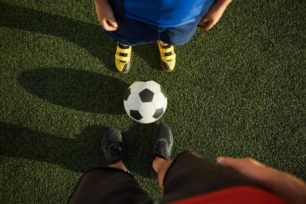 Father and son child playing football on outdoor field. Focus on feet of adult and young soccer players - Photo, Image