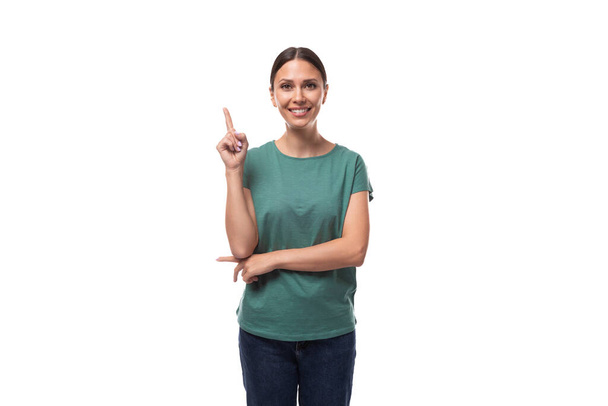 giovane donna snella e sicura vestita con una t-shirt verde basic con un mockup punta la mano verso l'annuncio. - Foto, immagini