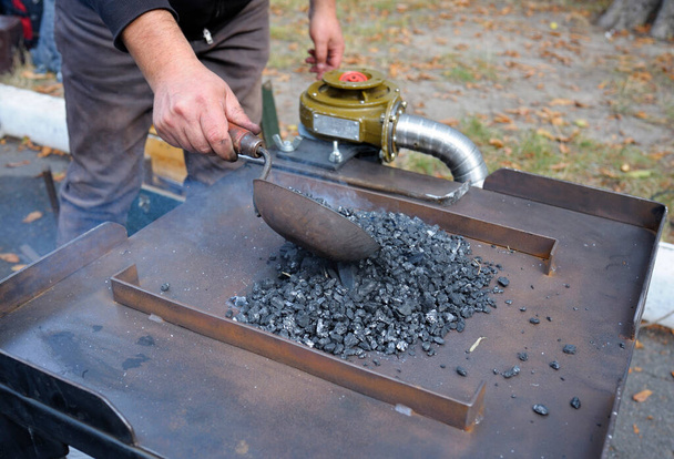 Blacksmith s hand adding coal to a burning forge with a scoop. At the smithy workshop. - Photo, Image