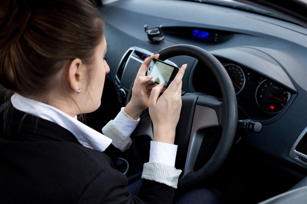 mujer de negocios utilizando el teléfono inteligente mientras conduce el coche
 - Foto, Imagen