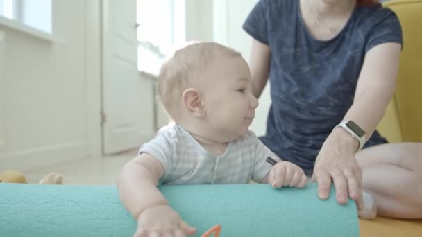 Küçük gülümseyen bir bebek kuklasını atıyor ve yoga minderini tutuyor. Orta çekim - Video, Çekim