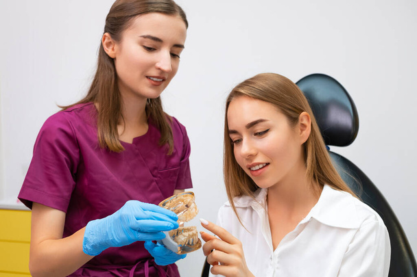 Kieferorthopäde erklärt die Vorgehensweise der Ausrichtung der Zähne auf den Patienten anhand eines Kiefergrundrisses in einer modernen Zahnklinik - Foto, Bild
