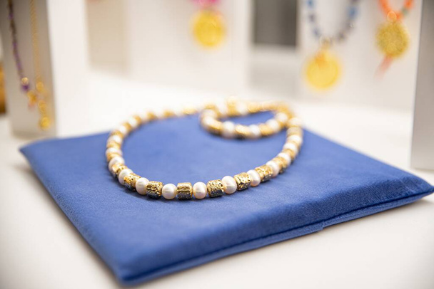Collar de perlas y cuentas de oro en un paño azul contra una pantalla de joyería borrosa - Foto, Imagen