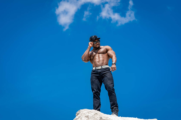 A shirtless man standing on top of a rock. A Rugged Adventurer Conquering Nature's Heights - Φωτογραφία, εικόνα