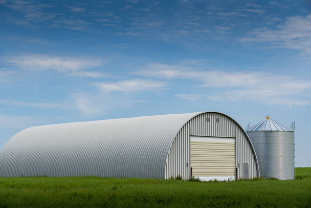 Farmyard quonset používá pro skladování zemědělských strojů s výhledem na obilí silo na kanadské prérie v Kneehole Země Alberta Kanada. - Fotografie, Obrázek