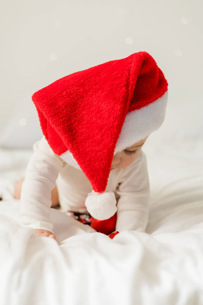 Bebé de Navidad en Santa Sombrero, Niño sosteniendo bauble de Navidad cerca de la caja de regalo presente sobre luces de vacaciones - Foto, imagen