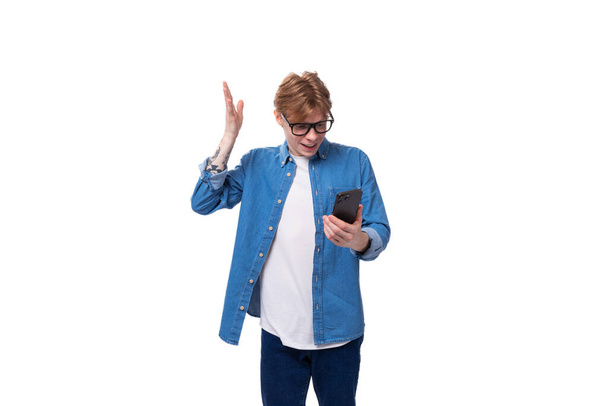 young smart european man with copper hair wears a denim shirt writes a message in the phone. - Photo, Image