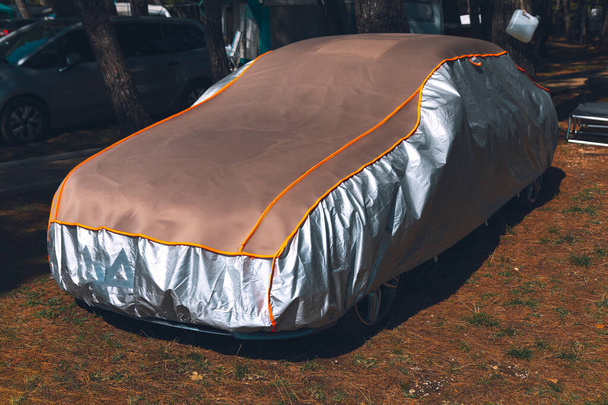 Car covered with tarp in parking area. Car beneath a protective tarp, surrounded by the tranquil beauty of nature - Photo, Image