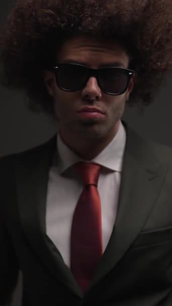 szexi üzletember elegáns fekete öltöny piros nyakkendő fogja a kezét a zsebében, és keres oldalán szürke háttér - Felvétel, videó