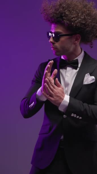 Cooler Mode-Bräutigam mit Sonnenbrille zur Seite blickend und Handflächen reiben vor buntem Hintergrund im Studio - Filmmaterial, Video