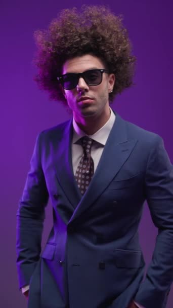 handsome elegant man in suit with big curly hair holding hands in pockets, looking to side and adjusting tie and suit on colorful background - Footage, Video