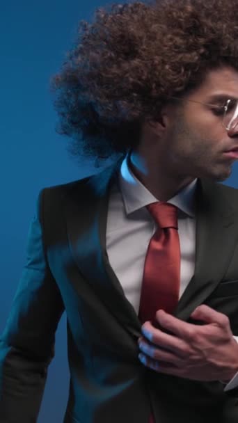 sexy fashion man with glasses looking to side, fixing suit and confidently looking forward when camera is closing up, making silence gesture on colorful background - Footage, Video