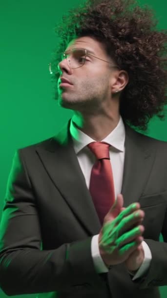 sebevědomý mladý muž v černém obleku s červenou kravatou dívá na stranu a tření dlaně, těšit a dát ruce v kapsách před barevným pozadím - Záběry, video