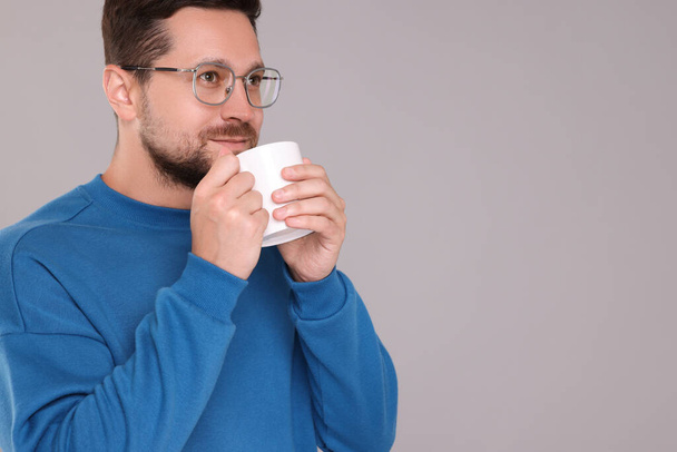 Man drinking from white mug on grey background. Space for text - Photo, image