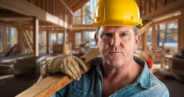 Contratista masculino en un sitio de construcción que usa un sombrero duro y guantes de trabajo que sostienen la madera 2x4  - Foto, imagen