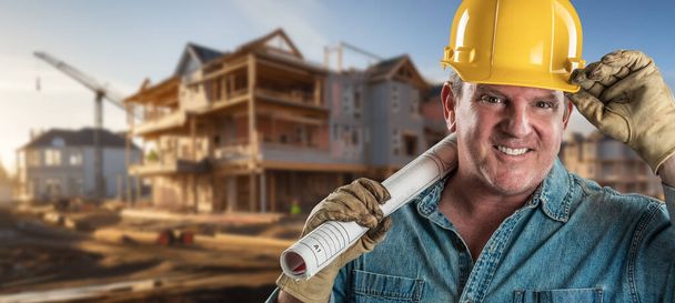 Vriendelijke mannelijke contractant op een bouwplaats dragen van een harde hoed en werkhandschoenen met zijn blauwdruk plan - Foto, afbeelding