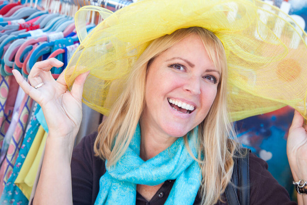Happy Blonde Woman Playfully Modeling a Big Sun Hat at the Market.  - Photo, Image