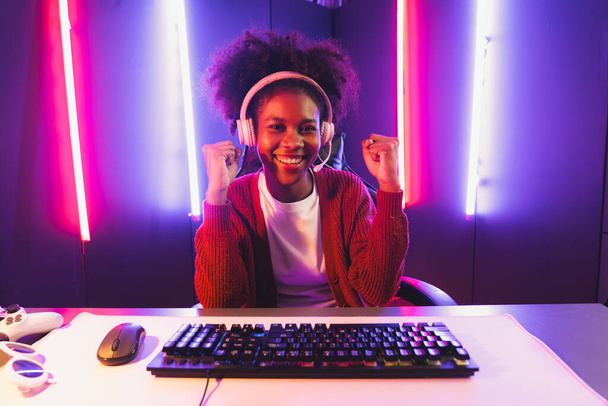 Gaming streamer, ragazza africana che gioca online combattendo con Esport squadra abile indossando cuffie nella stanza di illuminazione al neon colore. Parlare di altri giocatori che pianificano strategie per vincere i concorrenti. Tastificatore. - Foto, immagini
