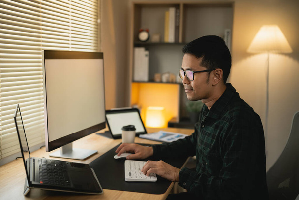 Okos ázsiai férfi mosolyog, szemüveget visel, számítógépes laptoppal dolgozik. koncepció munka otthon, maradj otthon. szabadúszó életstílus, új, normális társadalmi távolságtartó életmód. Munkaforma bárhol koncepció. - Fotó, kép