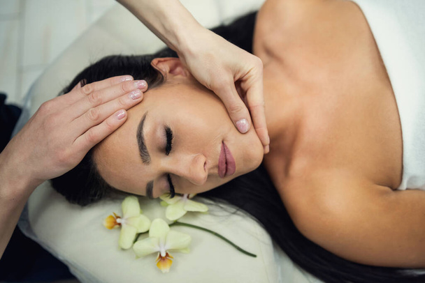 Młoda kobieta w salonie piękności mająca leczniczy masaż twarzy. Relaks masażu twarzy - Zdjęcie, obraz