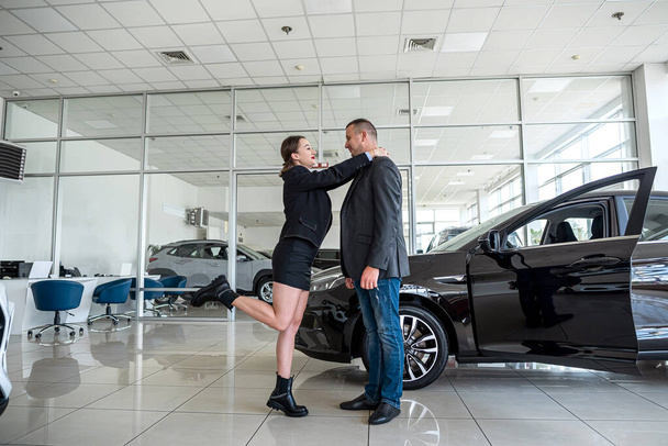 young couple buys a car at a car dealership and is sincerely happy about such a purchase. the concept of buying and selling a car. car dealership - Fotoğraf, Görsel