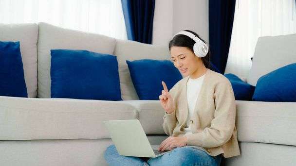 Jovem mulher asiática vestindo fone de ouvido enquanto trabalhava em laptop de computador em casa. Trabalho em casa, Videoconferência, Videochamada, Estudante aprendendo aula online - Foto, Imagem