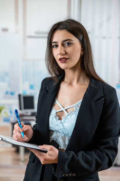 Muotokuva menestyneestä naissihteeristä puvussa pitämässä asiakirjoja sinkkuna toimistossa. Avustajan tai paperityön käsite - Valokuva, kuva