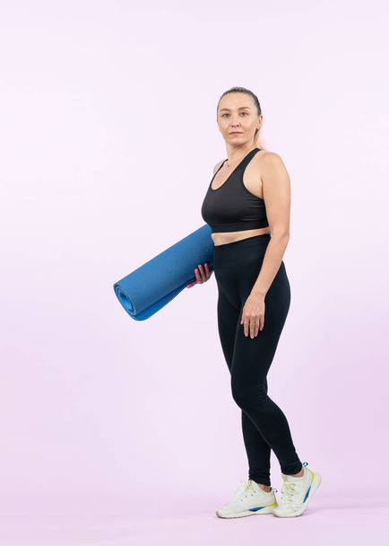 Full body length shot athletic and sporty senior woman holding fitness exercising mat on isolated background. Healthy active physique and body care lifestyle after retirement. Clout - Photo, Image