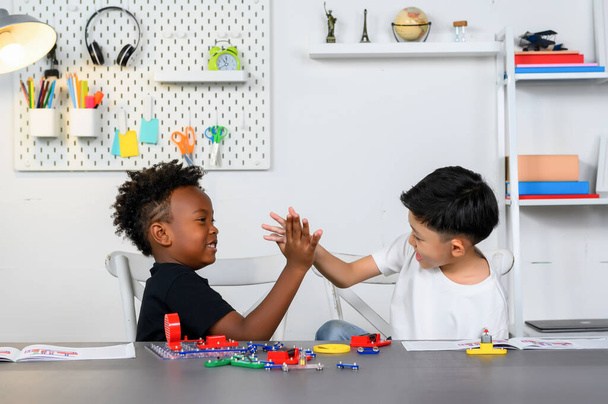 Two Children of different ethnicities high-fived each other after completing a collaborative project on electrical circuits. Children were proud of their accomplishments and Brainstormed ideas. - Photo, Image
