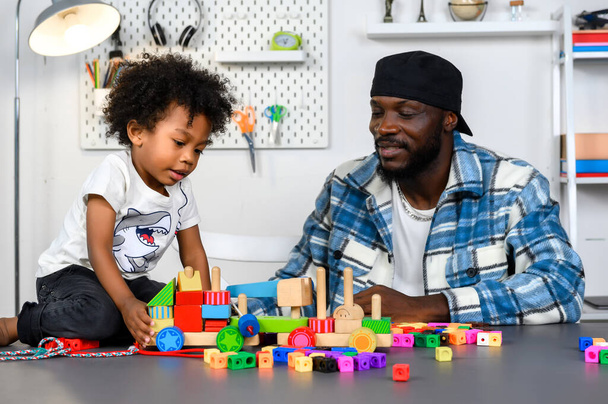 Szerető atya tanít és játszik a kisfiúval otthon a készségfejlesztéshez a fa játékkal és színes kockával. Apa táplálja a gyermek készségek a játék és az oktatás koncepció. - Fotó, kép