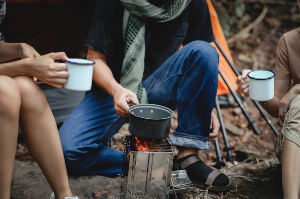 Detailní záběr vařící vody s vařičem v táboře skupiny mladých lidí na trekking, zatímco sedí v deštném pralese a popíjí kávu a vodu. - Fotografie, Obrázek