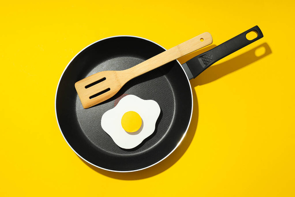 Τηγανίζουμε ένα αυγό σε ένα τηγάνι με μια ξύλινη σπάτουλα. - Φωτογραφία, εικόνα