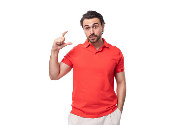 jong knappe brunette man in rood t-shirt gebaren op witte achtergrond met kopieerruimte. - Foto, afbeelding