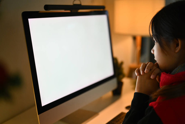 Seitenansicht junge Frau schaut auf einen leeren Computerbildschirm, der Videokurs oder Arbeit von zu Hause aus anschaut. - Foto, Bild