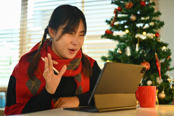 Fröhliche junge Frau beim Videoanruf per digitalem Tablet am geschmückten Weihnachtsbaum. - Foto, Bild