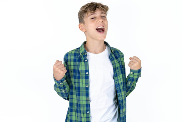 menino adolescente bonito vestindo camisa xadrez sobre fundo branco comemorando surpreso e surpreso com o sucesso com os braços levantados e os olhos fechados. Conceito de vencedor. - Foto, Imagem